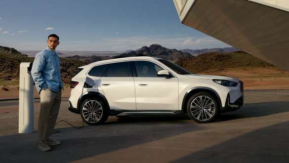 BMW iX1 U11 BEV 2022, cargando BMW iX1 U11 BEV 2022 Mineral White metalizado, vista de tres cuartos del lateral, aparcamiento en la entrada del garaje