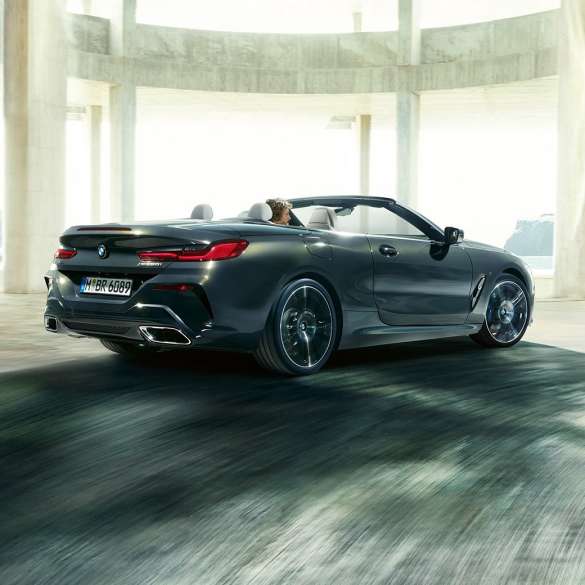 BMW M850i xDrive Cabrio, vista de tres cuartos de la zaga F91. BMW M850i xDrive Cabrio en Dravitgrau metalizado con la capota abierta, vista de tres cuartos de la zaga, atravesando un edificio de hormigón F91.