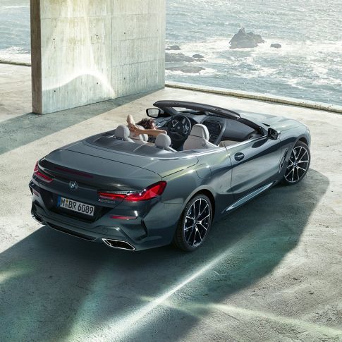 BMW M850i xDrive Cabrio, vista aérea F91. BMW M850i xDrive Cabrio en Dravitgrau metalizado con la capota abierta, vista aérea, aparcamiento en un edificio de hormigón situado frente al mar F91.