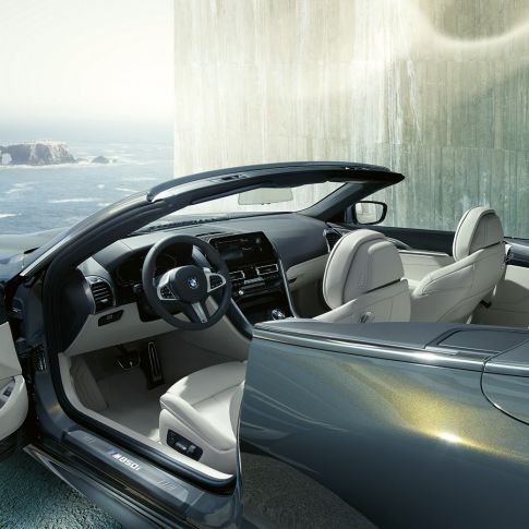 BMW M850i xDrive Cabrio, interior F91 BMW M850i xDrive Cabrio en Dravitgrau metalizado con la capota abierta, interior con volante de cuero M y equipamiento de cuero Merino BMW Individual en Elfenbeinweiss F91.