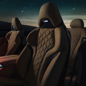 Asientos deportivos M en cuero Merino F91. BMW M8 Competition Cabrio con la capota abierta bajo un cielo estrellado, interior con asientos deportivos M en cuero Merino y luz ambiente roja F91.