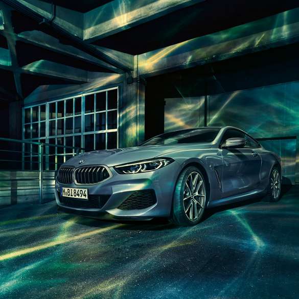 BMW M850i xDrive Coupé, vista de tres cuartos del frontal. BMW M850i xDrive Coupé en Barcelona Blau metalizado, vista de tres cuartos del frontal, parado delante de un edificio.