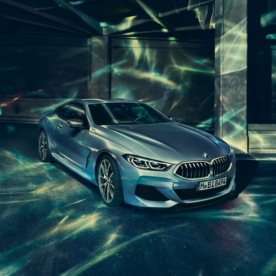 BMW M850i xDrive Coupé, vista de tres cuartos del frontal desde la izquierda. BMW M850i xDrive Coupé en Barcelona Blau metalizado, vista de tres cuartos del frontal desde la izquierda, parado delante de un edificio.
