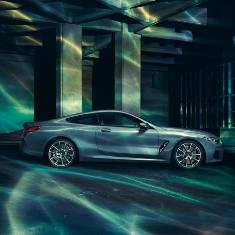 BMW M850i xDrive Coupé, vista del lateral. BMW M850i xDrive Coupé en Barcelona Blau metalizado, vista del lateral, parado delante de un edificio.