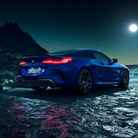 BMW M8 Competition Coupé, vista de tres cuartos de la zaga. BMW M8 Competition Coupé en Marina Bay Blau metalizado con las luces traseras LED encendidas, vista de tres cuartos de la zaga, parado bajo la luna llena.