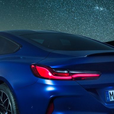Alerón trasero M. BMW M8 Competition Coupé en Marina Bay Blau metalizado, detalle de la línea de cintura con alerón trasero M en Carbonschwarz, de noche.