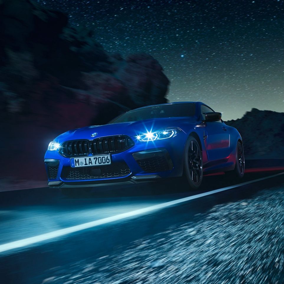 BMW M8 Competition Coupé, vista de tres cuartos del frontal. BMW M8 Competition Coupé en Marina Bay Blau metalizado con los faros LED encendidos, vista de tres cuartos del frontal, en marcha, por la noche.