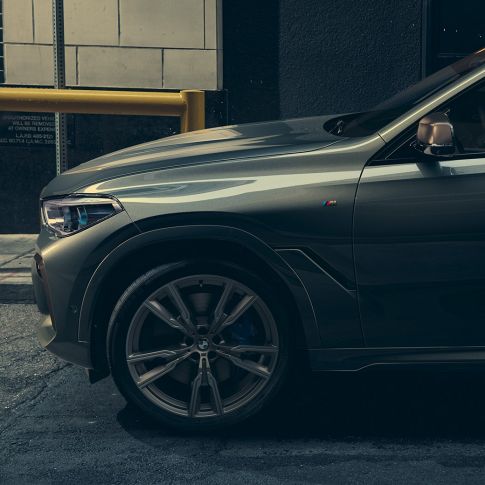 BMW X6 M50i en perspectiva lateral Hombre apoyado en el BMW X6 M50i en perspectiva lateral en un entorno urbano