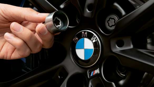 Dispositivo de seguridad para tornillos de ruedas BMW La mano indica el dispositivo de seguridad para tornillos de ruedas BMW delante de una rueda BMW