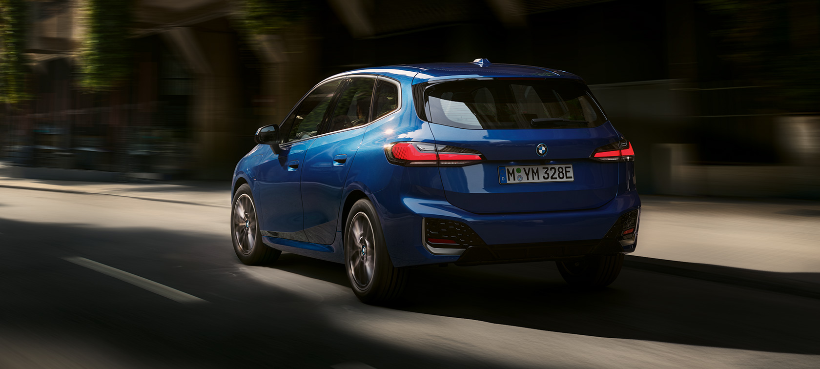 BMW Serie 2 Active Tourer 230e Híbrido Enchufable U06 2021 en marcha por la ciudad BMW Serie 2 Active Tourer 230e Híbrido Enchufable U06 2021 M Portimao Blue metalizado, vista de tres cuartos de la zaga, en marcha por la ciudad