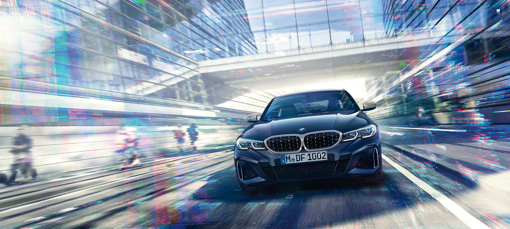 BMW Serie 3 Berlina, vista frontal del BMW M340i xDrive. Vista frontal del BMW M340i xDrive Berlina en marcha entre edificios urbanos de cristal.