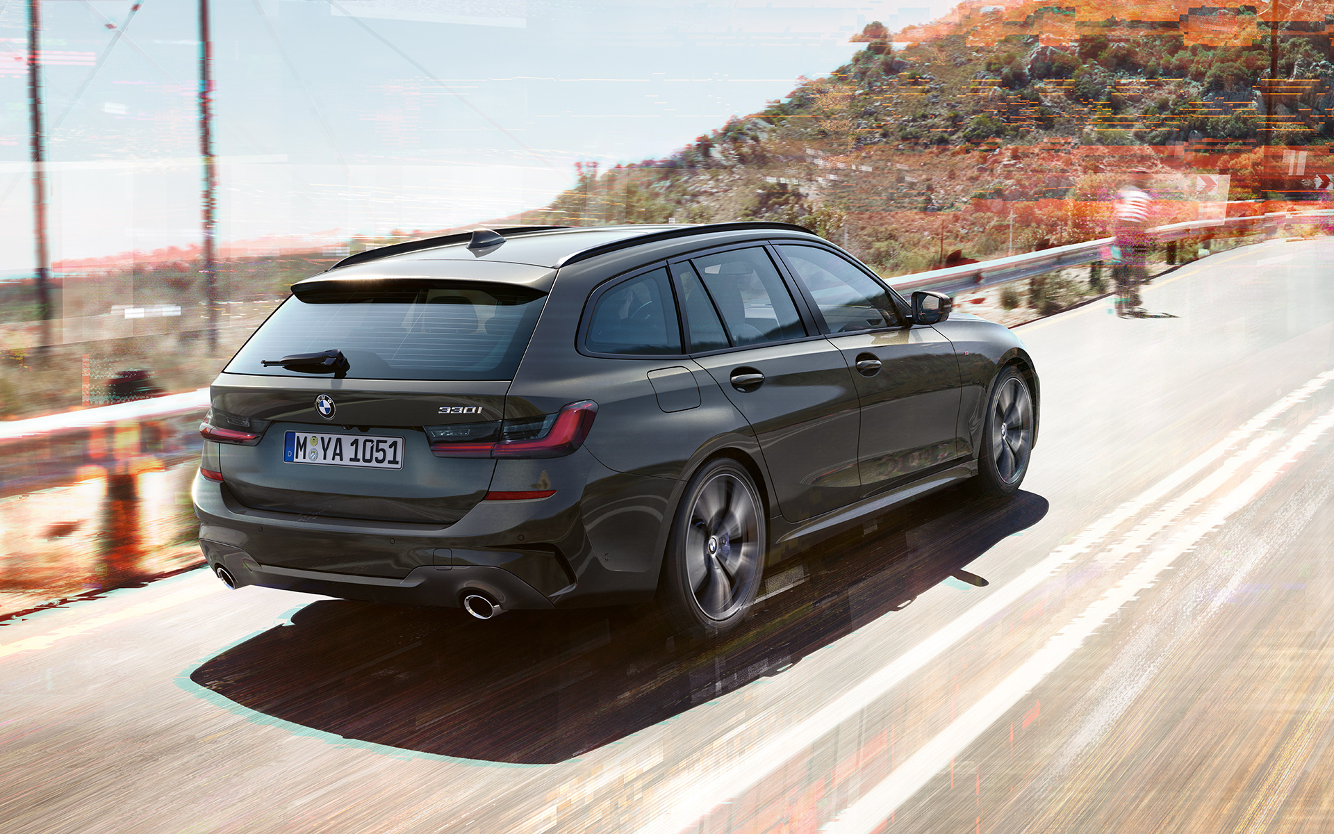 BMW Serie 3 Touring (G21), Dravit Grey, toma de tres cuartos de la zaga del vehículo en marcha sobre un puente delante de un entorno rural BMW Serie 3 Touring (G21), Dravit Grey, toma de tres cuartos de la zaga del vehículo en marcha sobre un puente delante de un entorno rural
