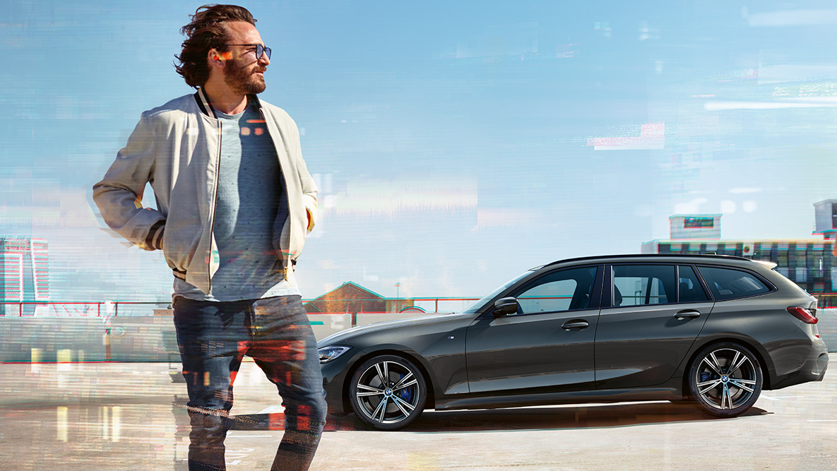 BMW Serie 3 Touring (G21), toma de tres cuartos del frontal, diseño BMW Serie 3 Touring (G21) Dravit Grey, toma de tres cuartos del frontal del vehículo en marcha sobre un puente delante de un entorno rural