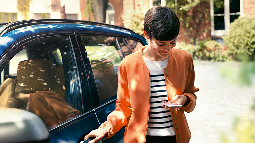 BMW Service Mujer con smartphone junto a la puerta de su BMW BMW Service Mujer con smartphone junto a la puerta de su BMW