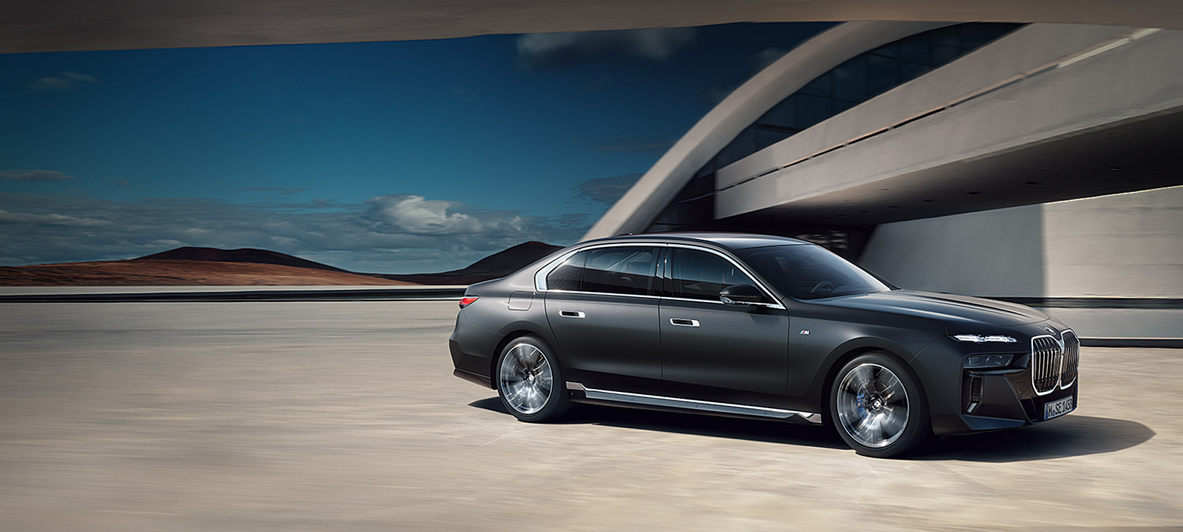 BMW Serie 7 G70 ICE Paquete M Sport, Frozen Deep Grey metalizado, vista de ¾ del frontal, parado delante de un edificio