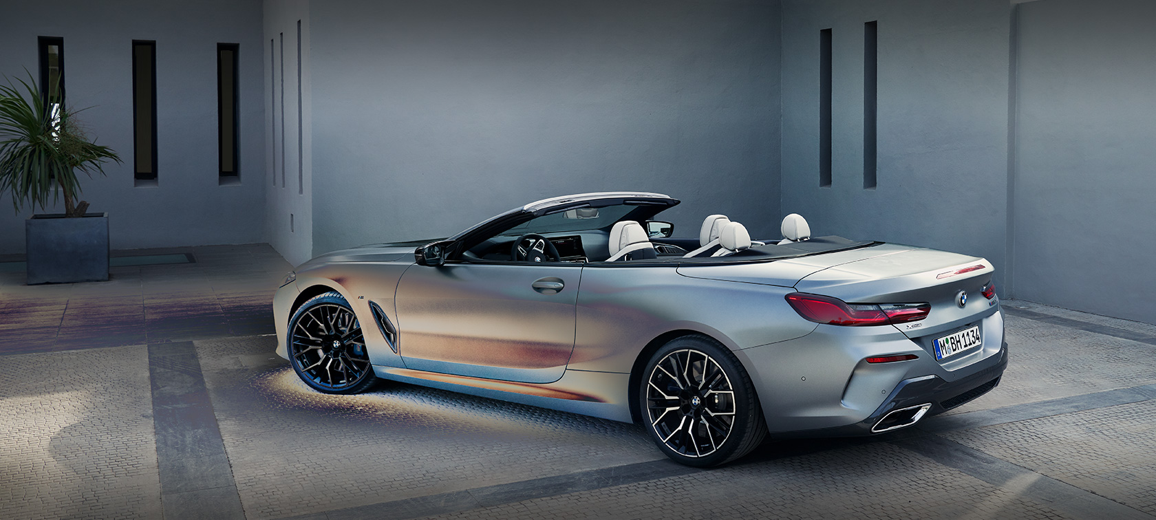 Hombre apoyado en un BMW Serie 8 Cabrio G14 LCI Renovación 2022 BMW Individual BMW Individual Frozen Pure Grey metalizado, vista lateral, parado, ante un edificio