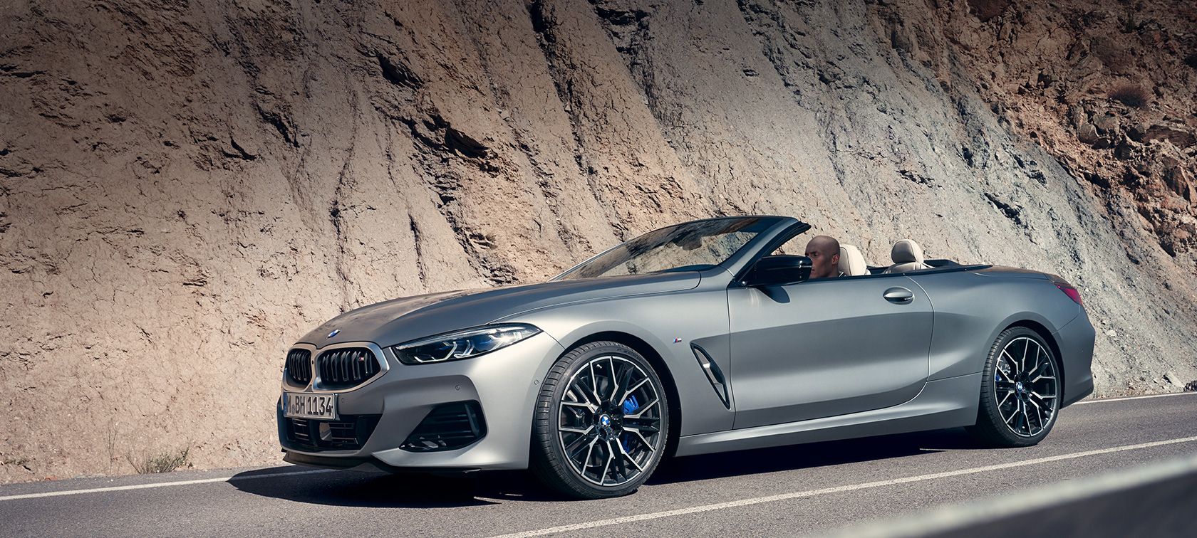 BMW Serie 8 Cabrio G14 LCI Renovación 2022 con capota abierta, en marcha, junto a la montaña BMW Serie 8 Cabrio G14 LCI Renovación 2022 BMW Individual Frozen Pure Grey metalizado, vista lateral, con capota abierta, en marcha, junto a la montaña
