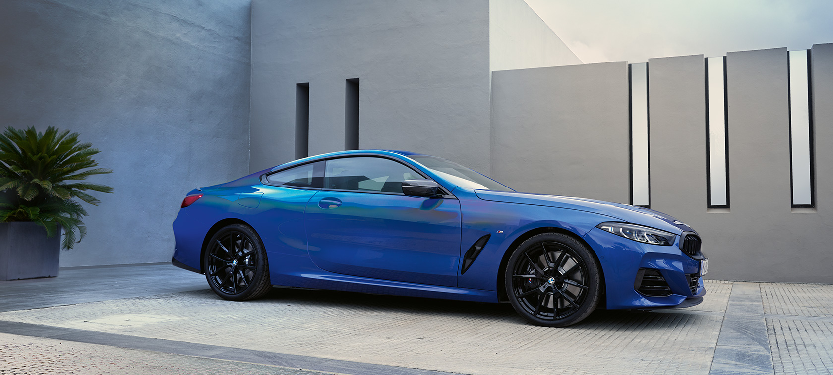 BMW Serie 8 Coupé G15 LCI Renovación 2022 M Portimao Blue metalizado, vista lateral, parado, ante la pared de una casa