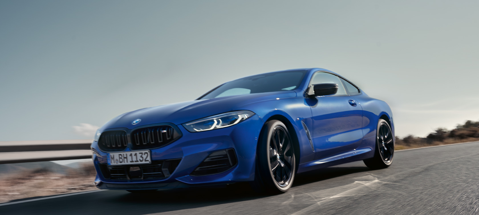 BMW Serie 8 Coupé G15 LCI Renovación 2022 BMW M850i xDrive M Portimao Blue metalizado, vista del frontal, perspectiva desde ángulo inferior BMW Serie 8 Coupé G15 LCI Renovación 2022 BMW M850i xDrive M Portimao Blue metalizado, vista del frontal en perspectiva desde ángulo inferior, en marcha, por carretera rural, con colinas al fondo