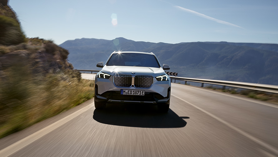 BMW iX1 U11 BEV 2022 vista del frontal BMW iX1 U11 BEV 2022 Mineral White metalizado, vista del frontal, carretera de montaña, en marcha