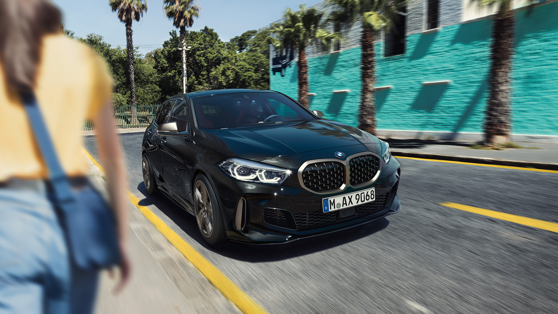 BMW M135i xDrive, vista frontal de tres cuartos BMW M135i xDrive en Black Sapphire metalizado, vista frontal de tres cuartos, con mujer en primer plano.
