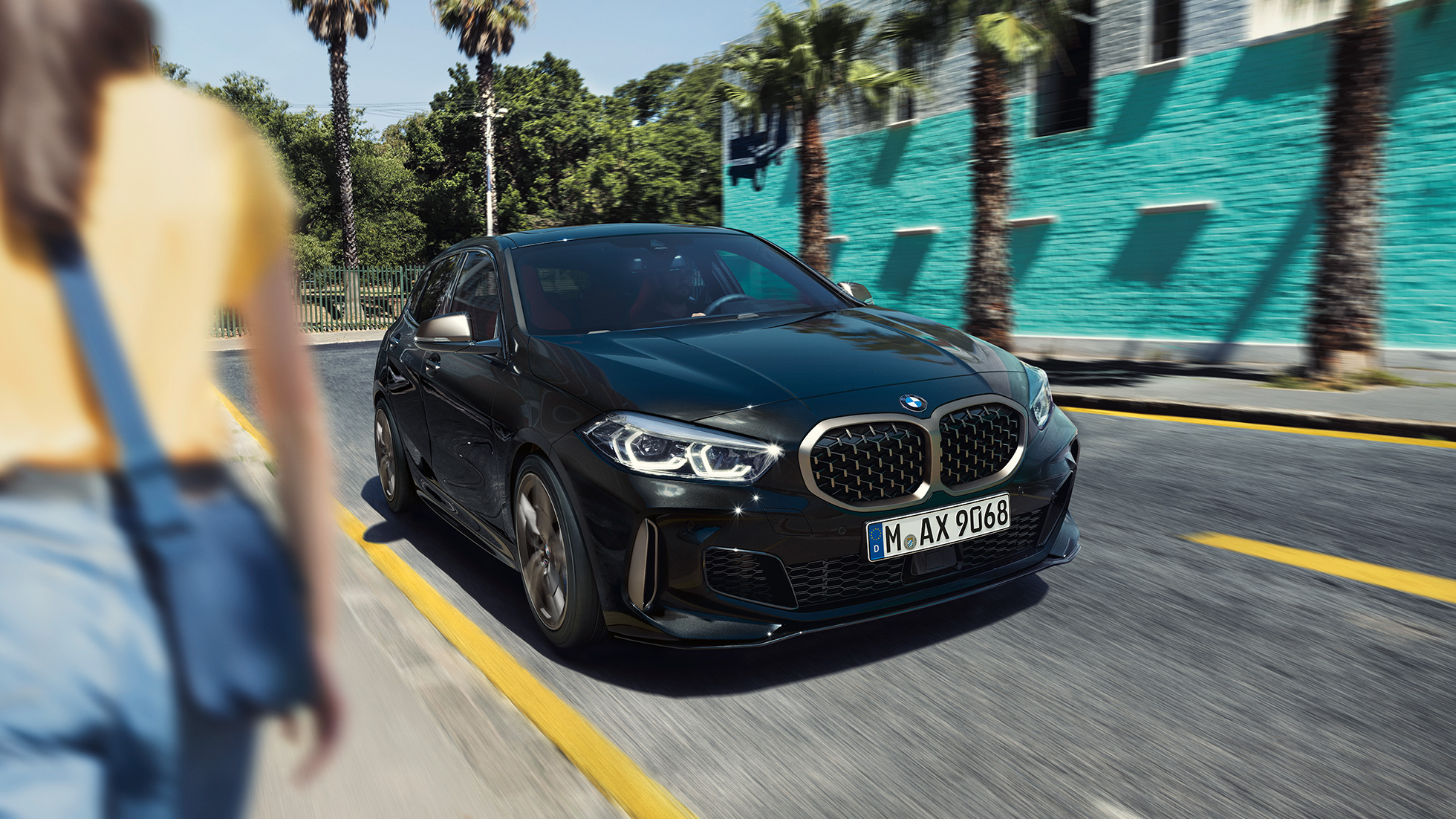 BMW M135i xDrive, vista frontal de tres cuartos BMW M135i xDrive en color Black Sapphire metalizado, vista frontal de tres cuartos, con mujer en primer plano.