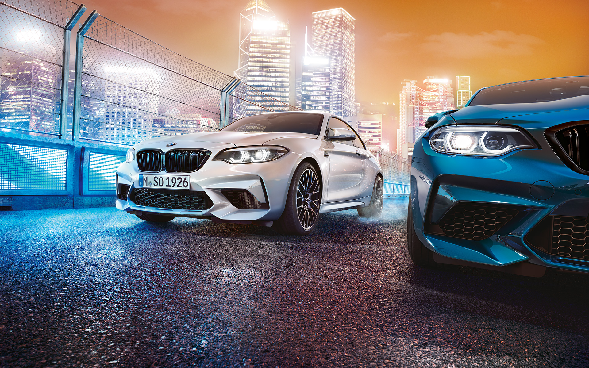Tres vehículos BMW M2 Competition en una vista frontal Tres vehículos BMW M2 Competition, con el perfil de la ciudad iluminado de fondo, en una vista frontal.
