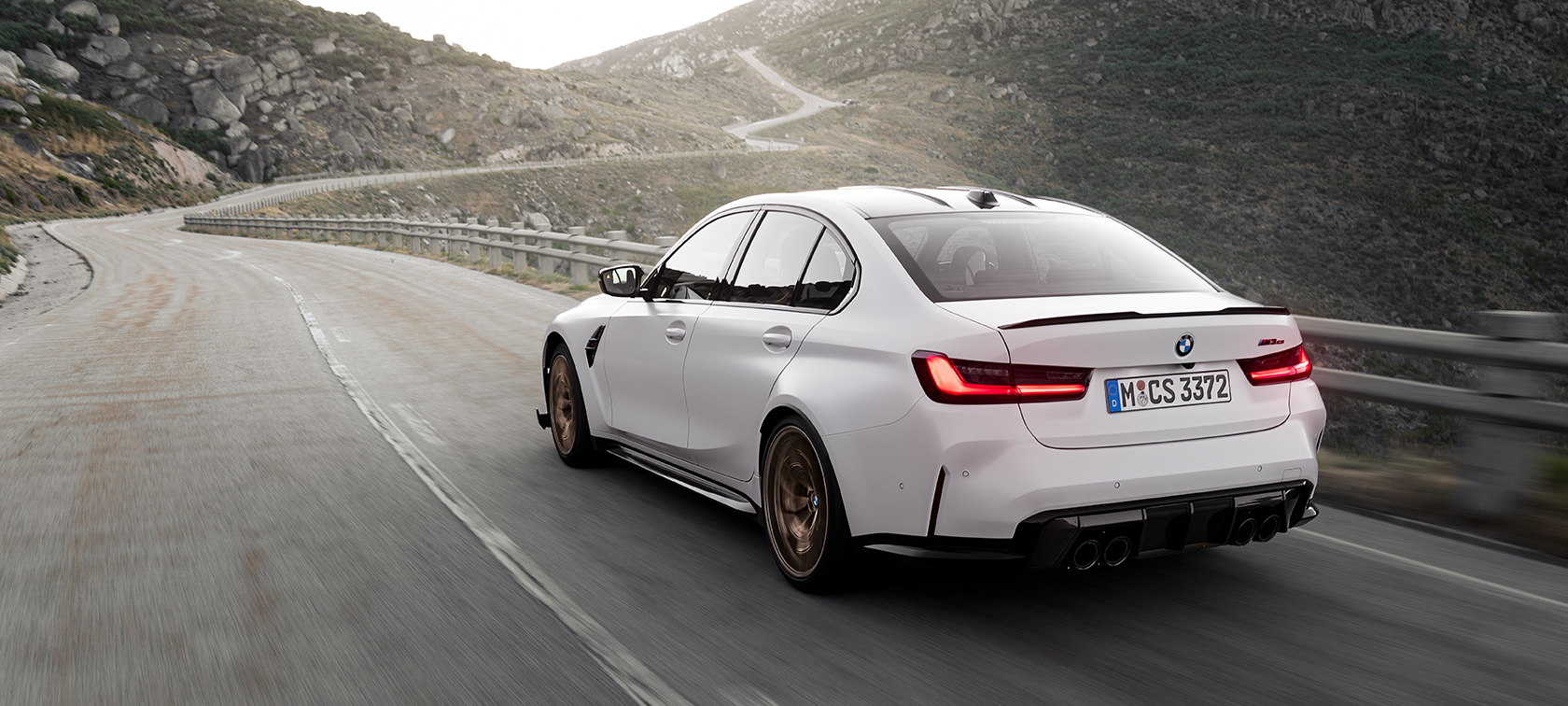 BMW M3 CS G80 Vista de tres cuartos de la zaga, en marcha BMW M3 CS G80 Vista de tres cuartos de la zaga circulando por una carretera de montaña