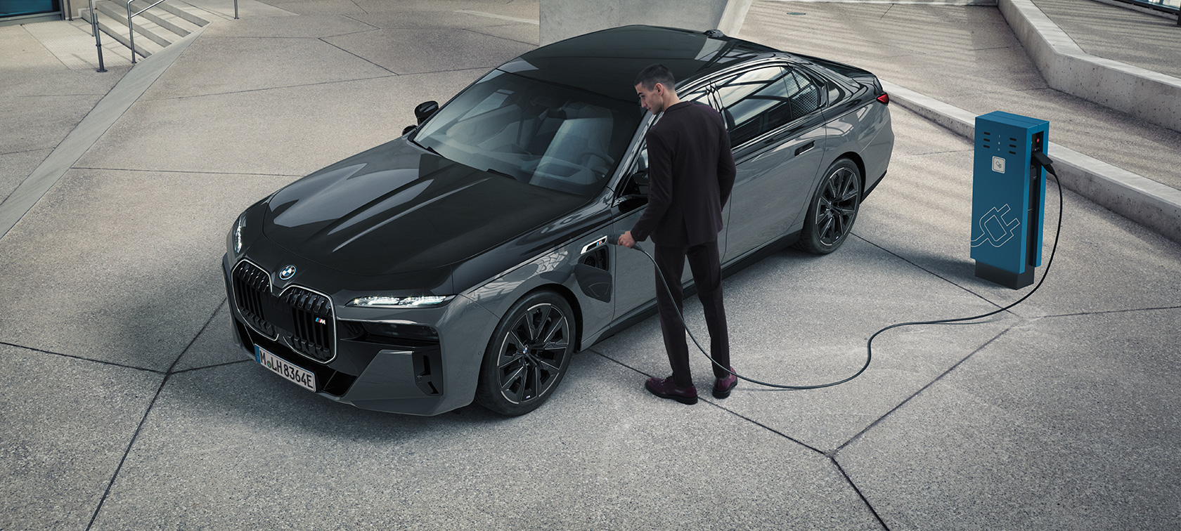 BMW M760e xDrive Berlina G70 Paquete M Performance Paquete BMW M760e xDrive Berlina G70 M Performance Pintura BMW Individual Black Sapphire metalizado bitono BMW Individual Dravit Grey metalizado, vista de tres cuartos del frontal, hombre con cable de carga junto al punto de carga