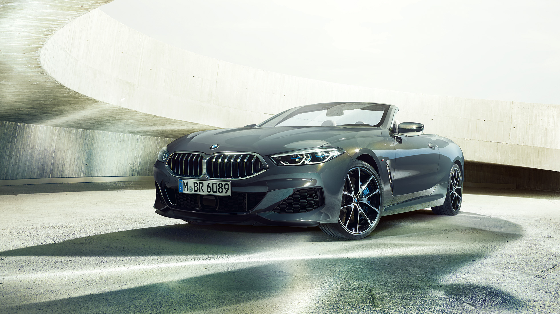 BMW M850i xDrive Cabrio, vista de tres cuartos del frontal F91. BMW M850i xDrive Cabrio en Dravitgrau metalizado con la capota abierta, vista de tres cuartos del coche deportivo descapotable F91
