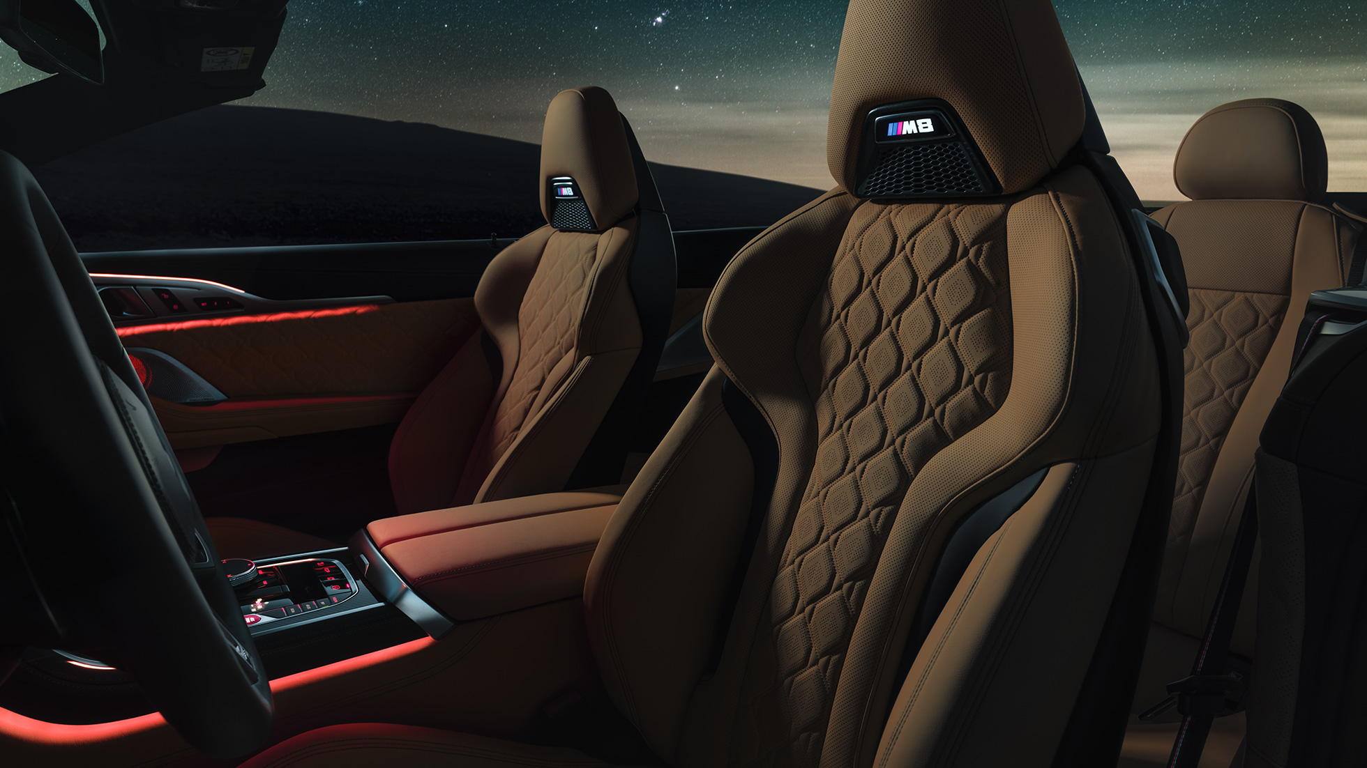 Asientos deportivos M en cuero Merino F91. BMW M8 Competition Cabrio con la capota abierta bajo un cielo estrellado, interior con asientos deportivos M en cuero Merino y luz ambiente roja F91.