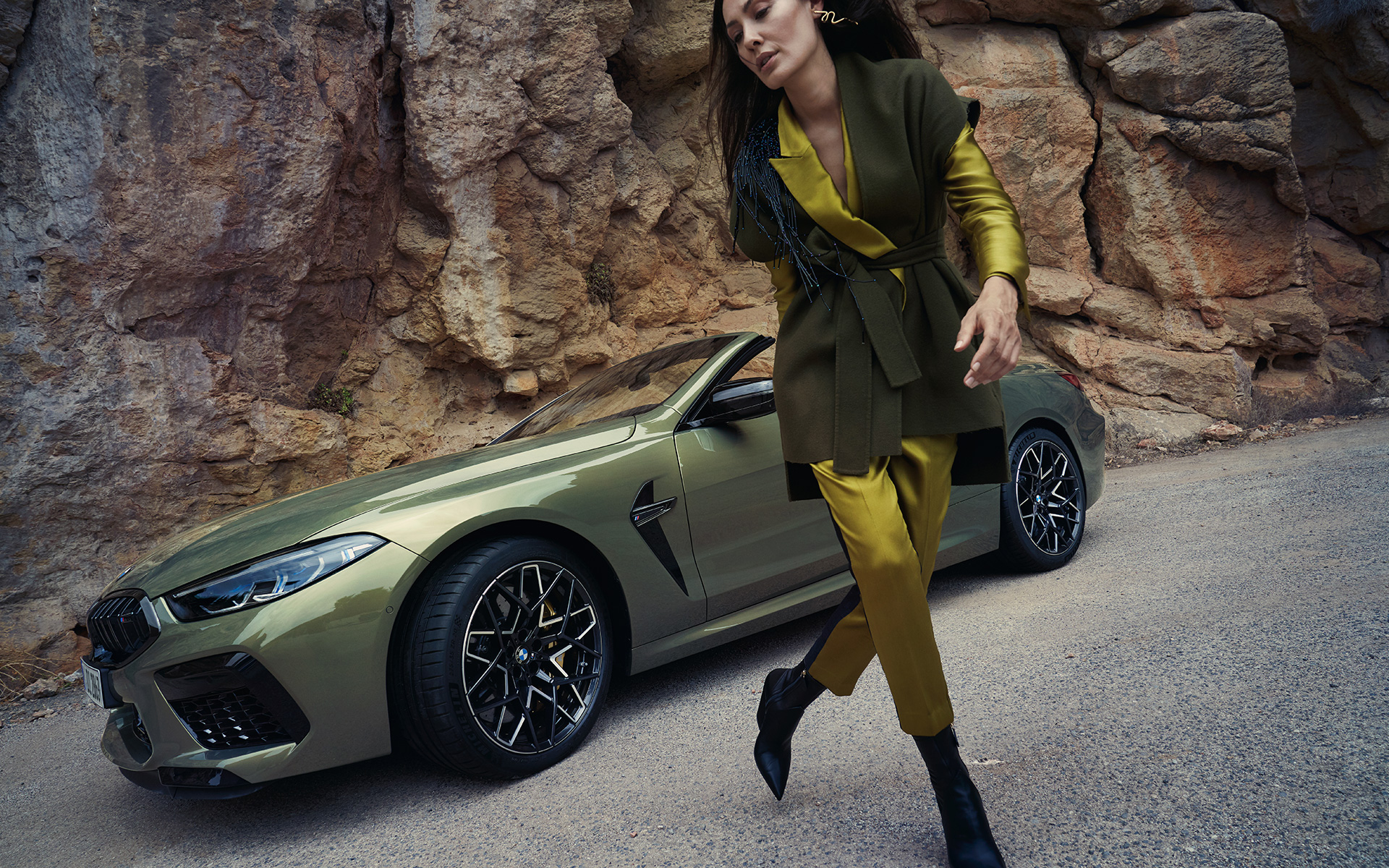 BMW M8 Competition Cabrio F91 LCI Renovación 2022 BMW Individual Brass metalizado, vista de tres cuartos del frontal, parado, en terreno pedregoso, con modelo femenina