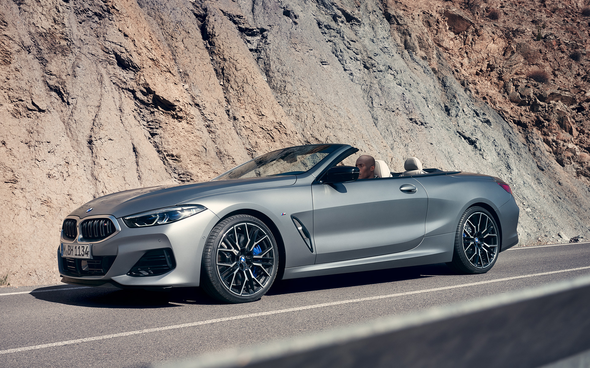BMW M850i xDrive Cabrio G14 LCI Renovación 2022 BMW Individual Frozen Pure Grey metalizado, vista de tres cuartos del frontal, en marcha, ante una pared de roca