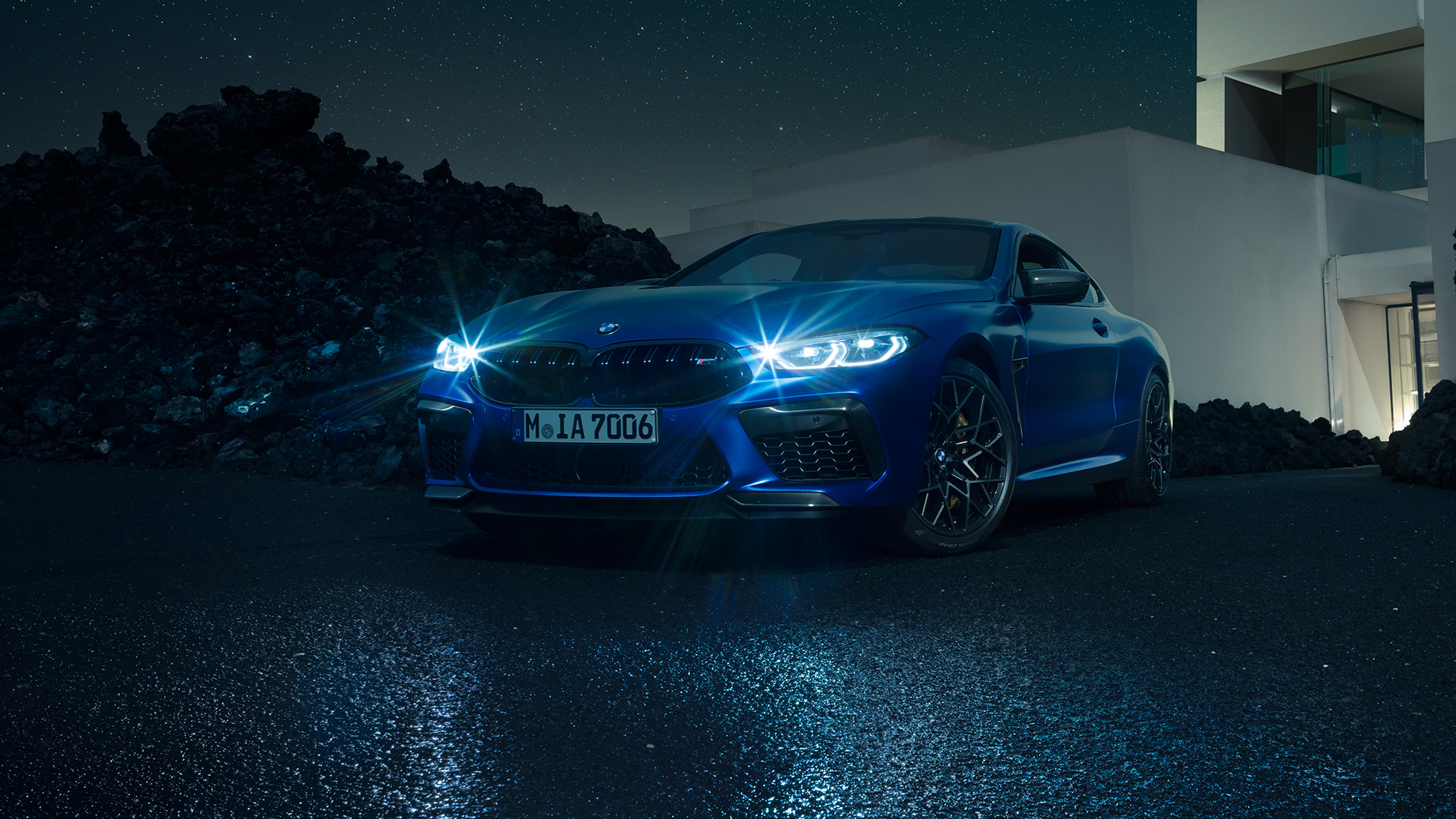 BMW M8 Competition Coupé, vista de tres cuartos del frontal. BMW M8 Competition Coupé en Marina Bay Blau metalizado con los faros LED encendidos, vista de tres cuartos del frontal, parado delante de una casa de campo, de noche.