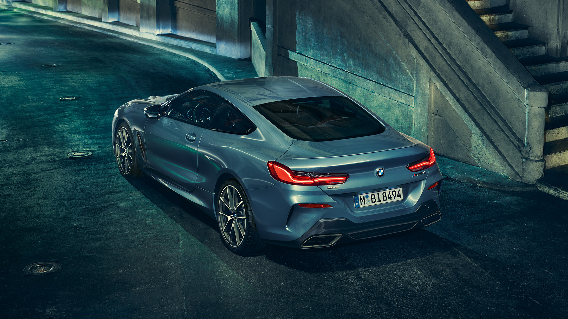 BMW M850i xDrive Coupé, vista de tres cuartos de la zaga desde la izquierda. BMW M850i xDrive Coupé en Barcelona Blau metalizado, vista de tres cuartos de la zaga desde la izquierda, parado, por la noche.