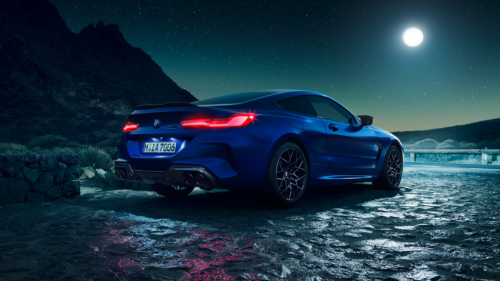 BMW M8 Competition Coupé, vista de tres cuartos de la zaga. BMW M8 Competition Coupé en Marina Bay Blau metalizado con las luces traseras LED encendidas, vista de tres cuartos de la zaga, parado bajo la luna llena.