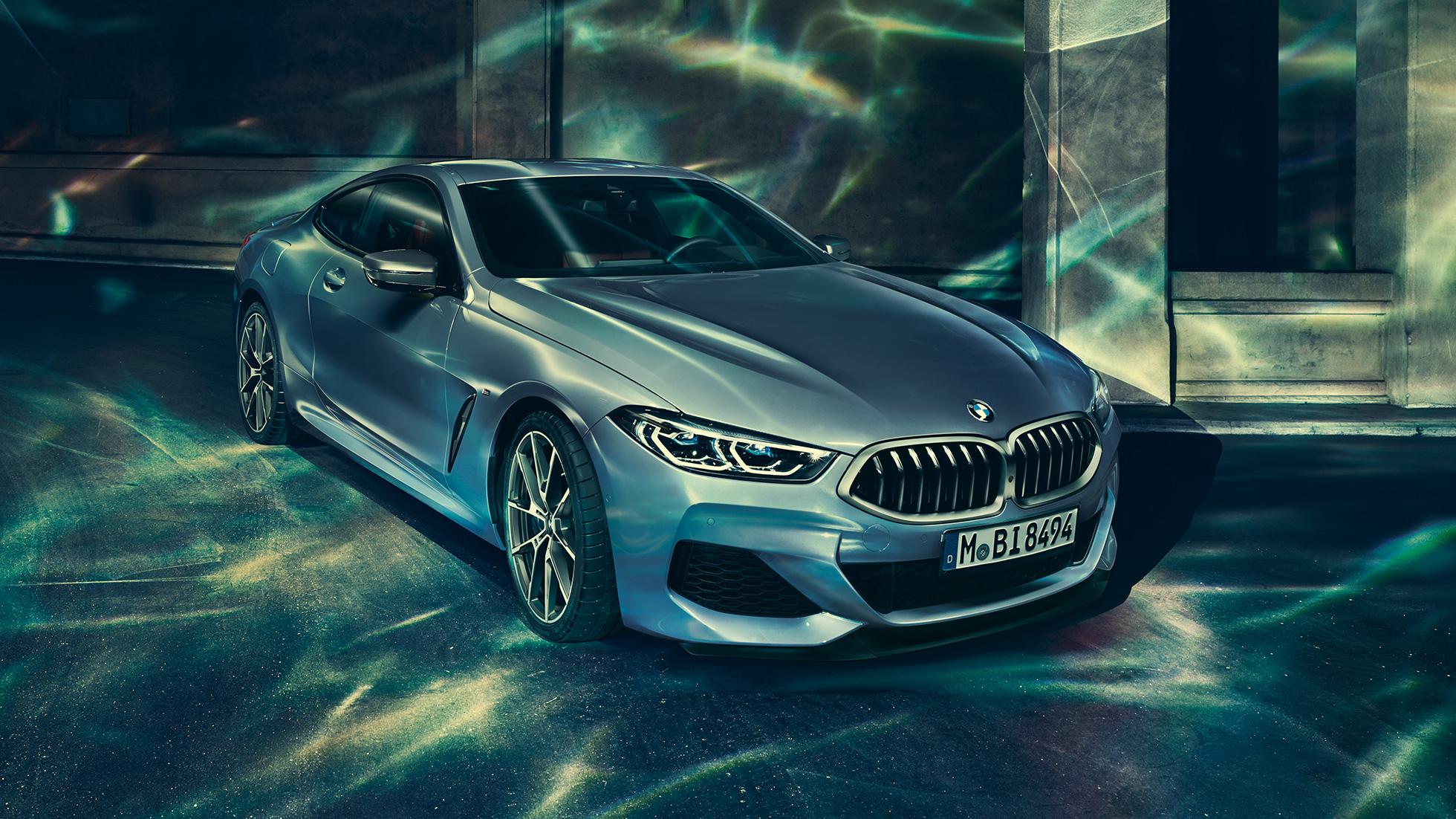 BMW M850i xDrive Coupé, vista de tres cuartos del frontal desde la izquierda. BMW M850i xDrive Coupé en Barcelona Blau metalizado, vista de tres cuartos del frontal desde la izquierda, parado delante de un edificio.