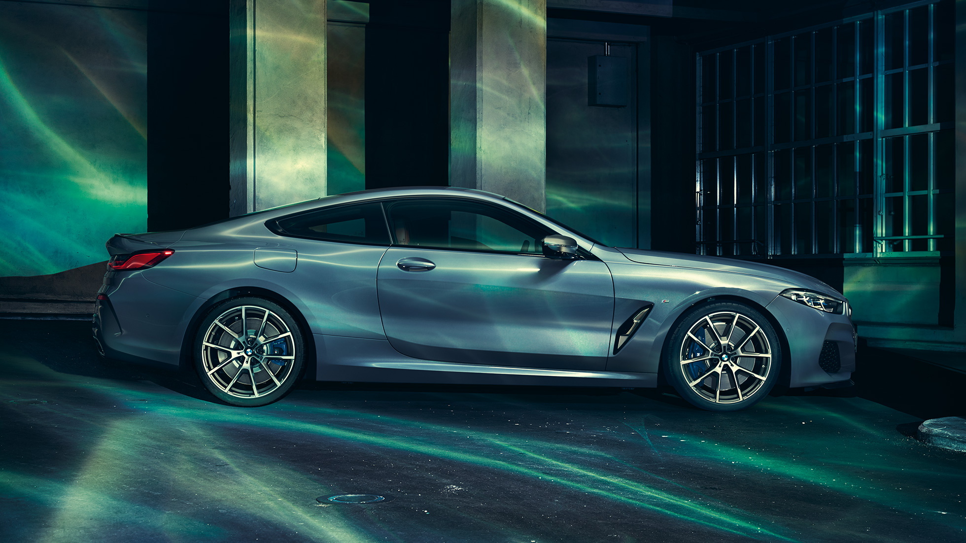 BMW M850i xDrive Coupé, vista del lateral. BMW M850i xDrive Coupé en Barcelona Blau metalizado, vista del lateral, parado delante de un edificio.
