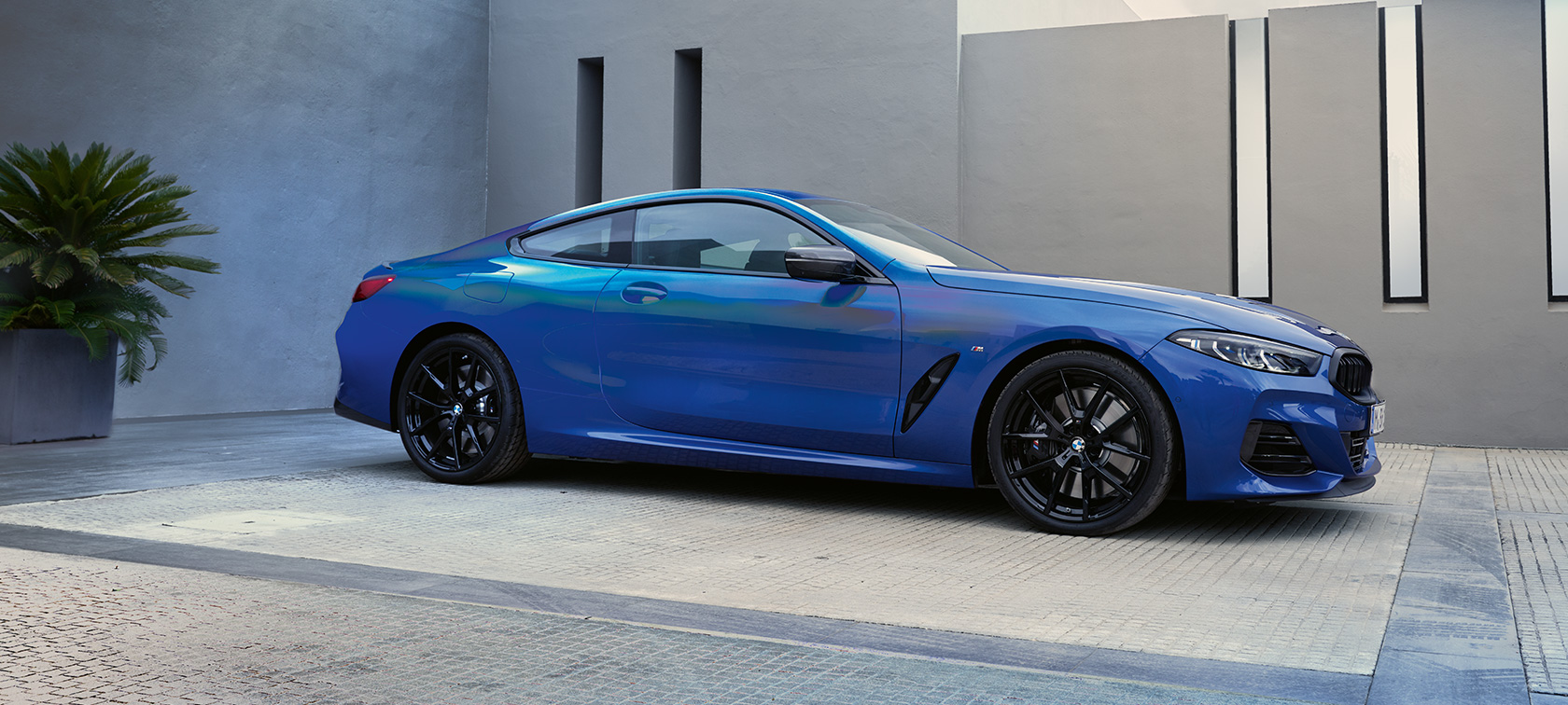 Vista lateral del BMW M850i xDrive Coupé G15 LCI Renovación 2022 BMW M850i xDrive Coupé G15 LCI Renovación 2022 M Portimao Blue metalizado, vista lateral, parado, ante un edificio