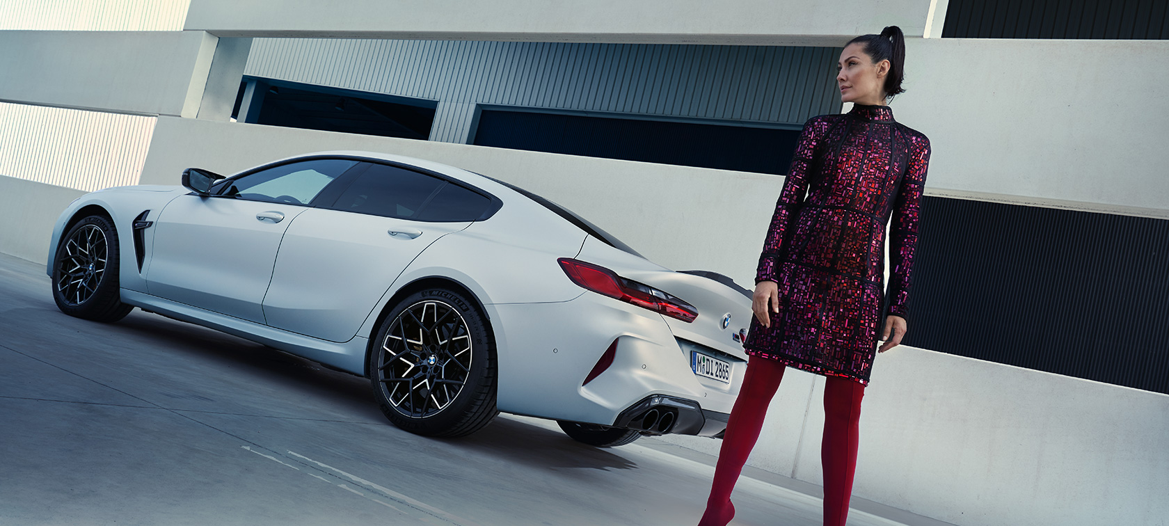 Vista de tres cuartos de la zaga BMW M8 Competition Gran Coupé F93 LCI 2022 BMW M8 Competition Gran Coupé F93 LCI Renovación 2022 BMW Individual Frozen Brilliant White metalizado, vista de tres cuartos de la zaga, con modelo femenina junto a un vehículo