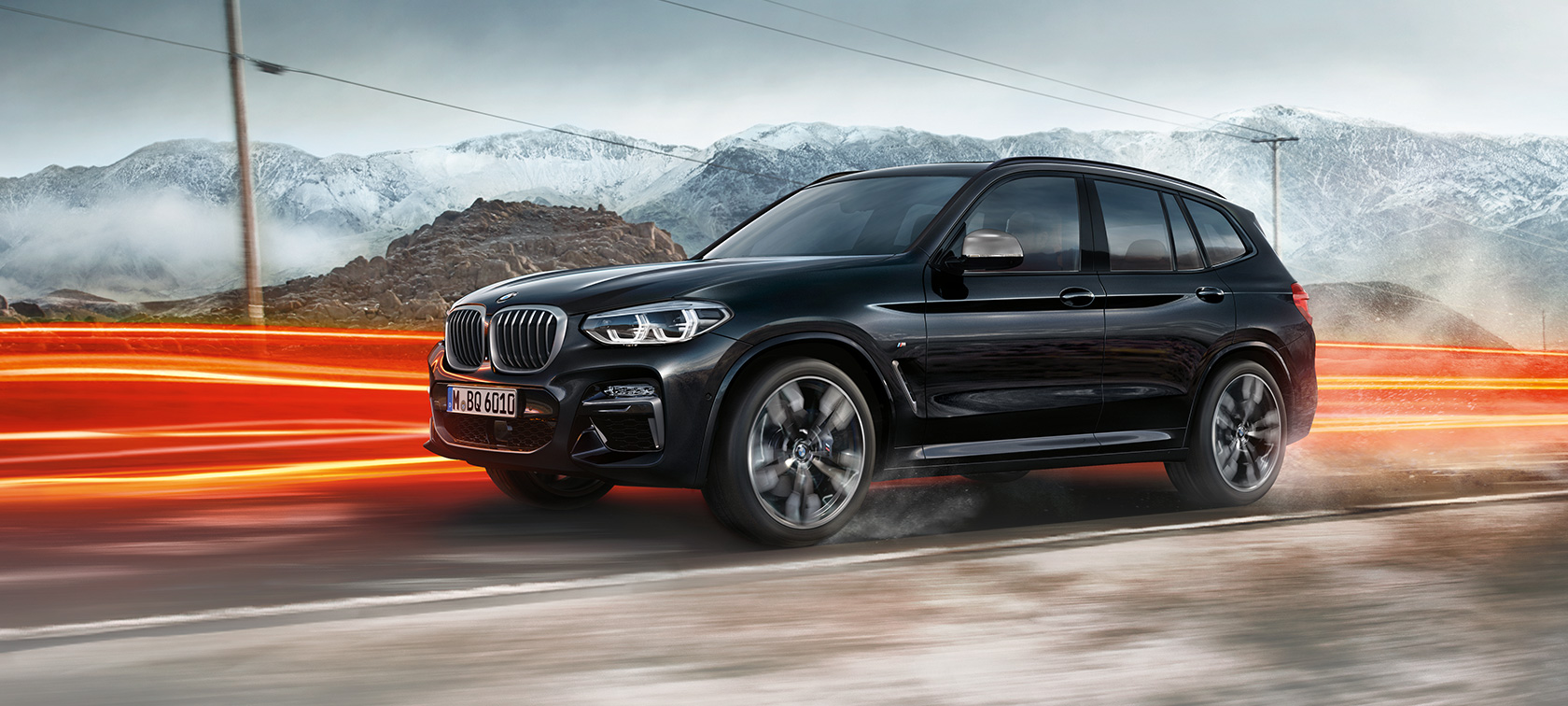 BMW X3 M40i y BMW X3 M40d, vista lateral BMW X3 M40i y BMW X3 M40d en Black Sapphire metalizado, conducción, exterior, vista lateral delante de un paisaje de montaña con bandas luminosas.