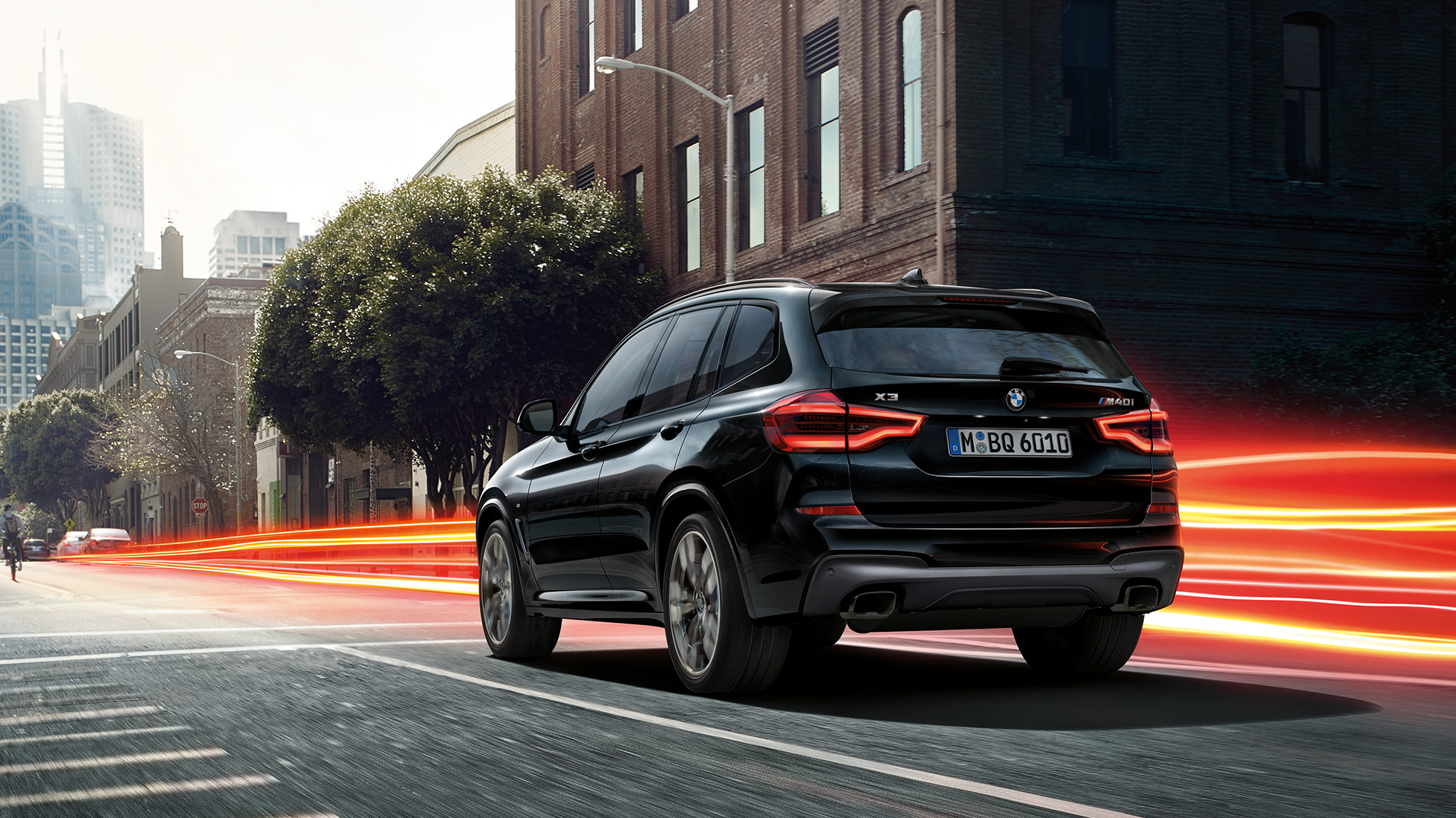 BMW X3 M40i, vista de tres cuartos de la zaga BMW X3 M40i en Black Sapphire metalizado, conducción, exterior, vista de tres cuartos de la zaga ante un fondo urbano con bandas luminosas.