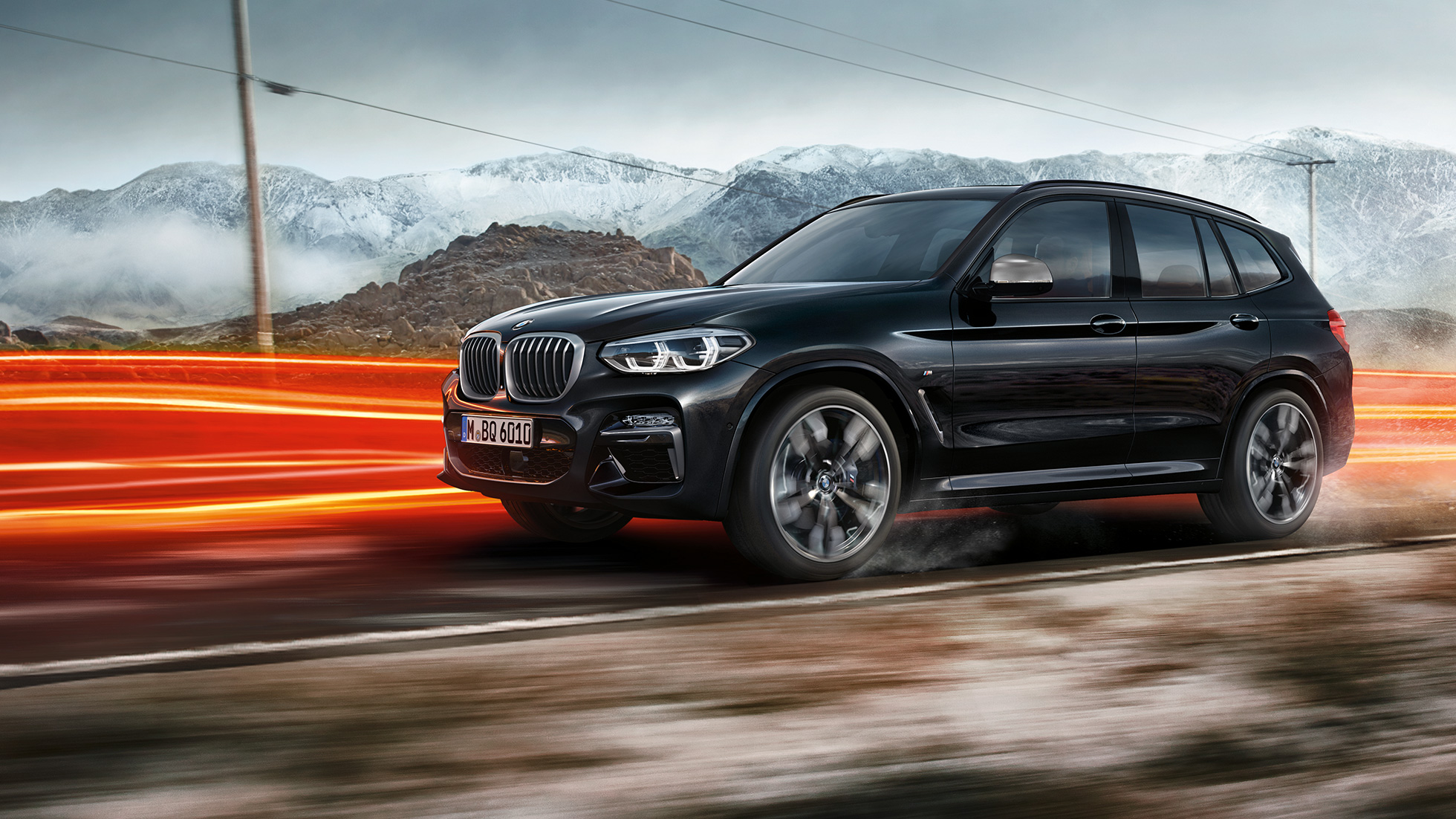 BMW X3 M40i y BMW X3 M40d, vista lateral BMW X3 M40i y BMW X3 M40d en Black Sapphire metalizado, conducción, exterior, vista lateral delante de un paisaje de montaña con bandas luminosas.