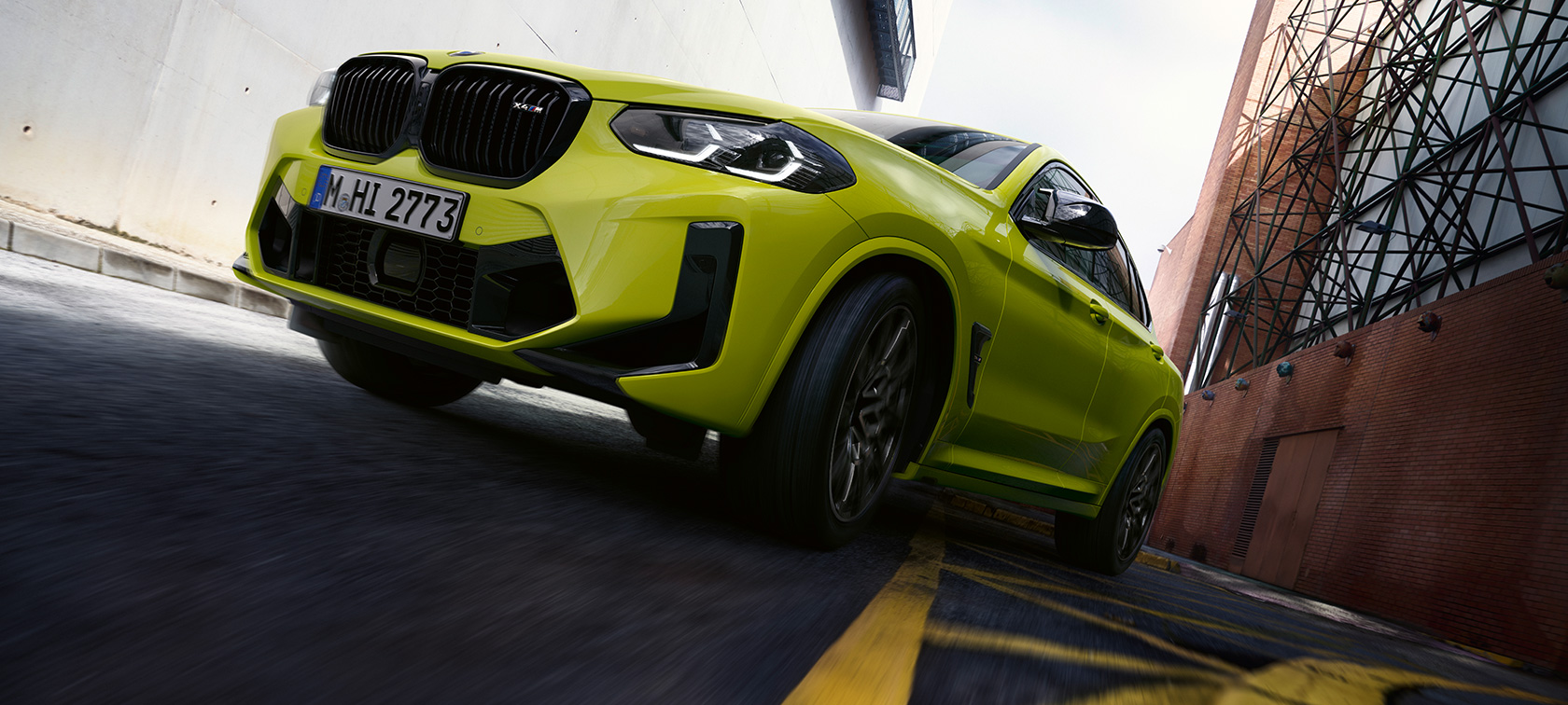 BMW X4 M Competition F98 LCI Renovación 2021 Sao Paulo Gelb Vista de tres cuartos del frontal con vista desde abajo circulando por un cañón urbano