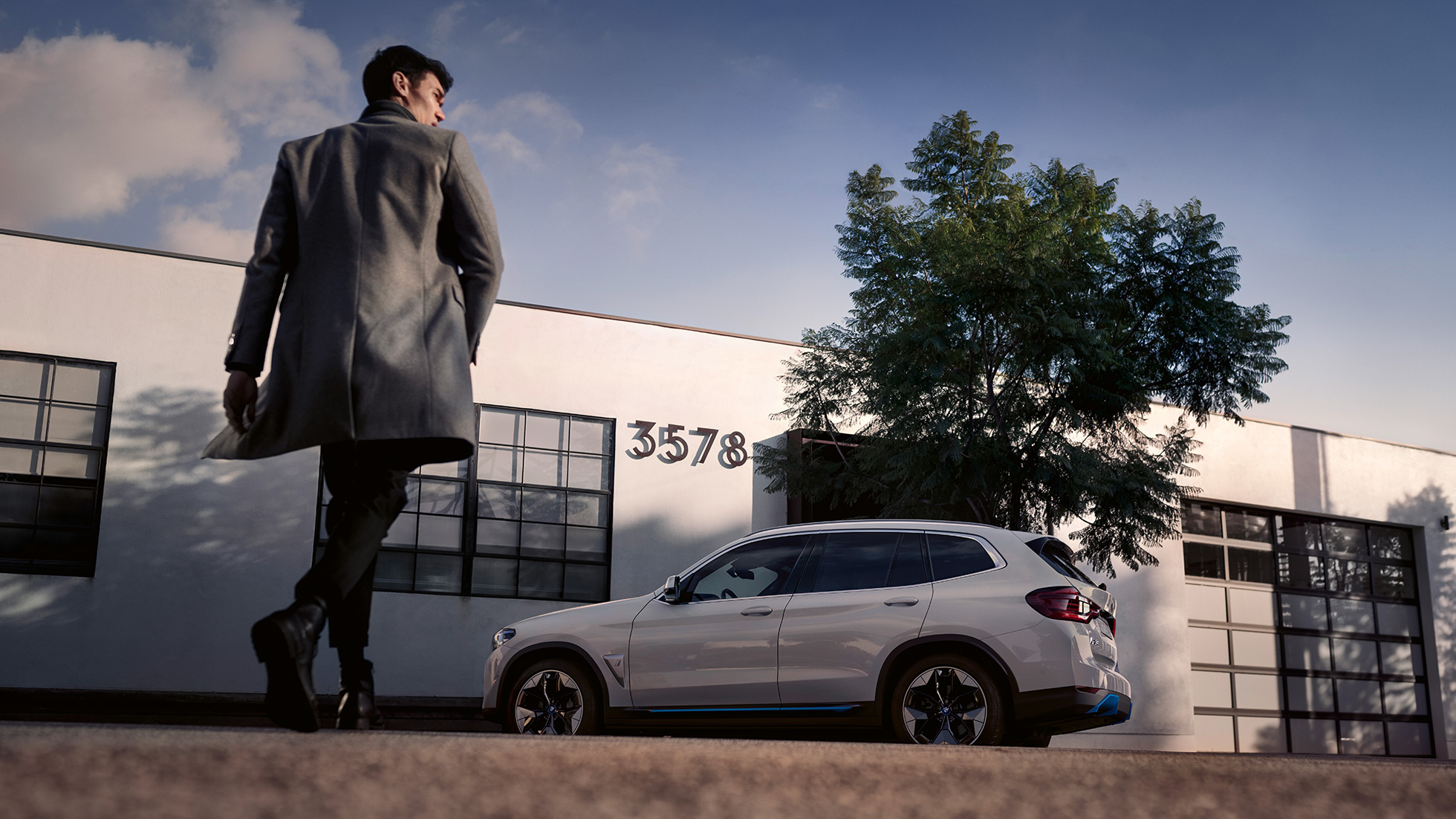 BMW iX3 G08 Vista lateral delante de edificio con un hombre BMW iX3 G08 2020 Mineralweiss metalizado Vista lateral delante de un edificio con un hombre