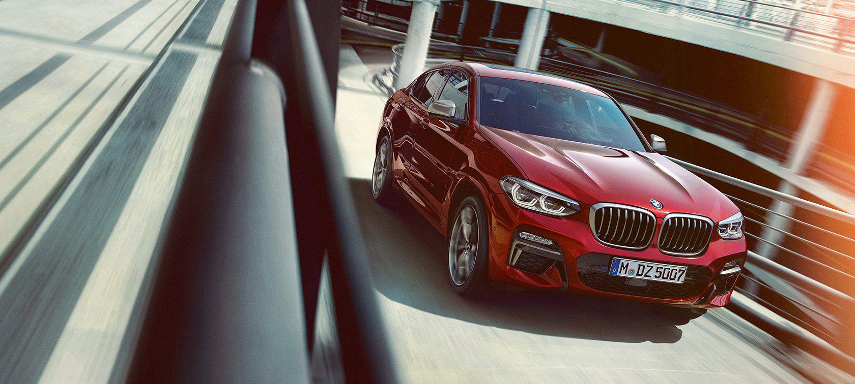 BMW X4 SUV G02 conducción en aparcamiento de varias plantas BMW X4 SUV G02, en color Flamencorot efecto brillante, vista de tres cuartos del lateral