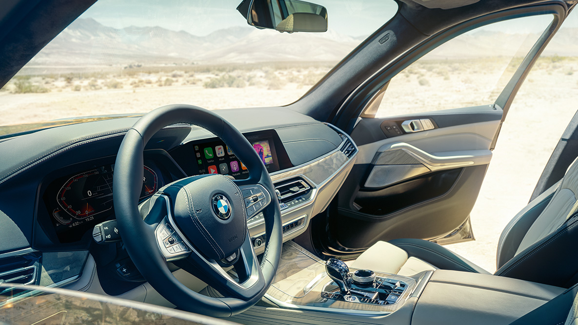 Interior del BMW X7 Interior del BMW X7: vista desde el exterior de la primera fila de asientos con el volante, el cuadro de instrumentos y los asientos de cuero