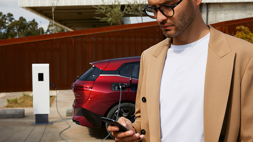Hombre con smartphone delante de un BMW iX en punto de carga Hombre con smartphone delante de un BMW iX en punto de carga