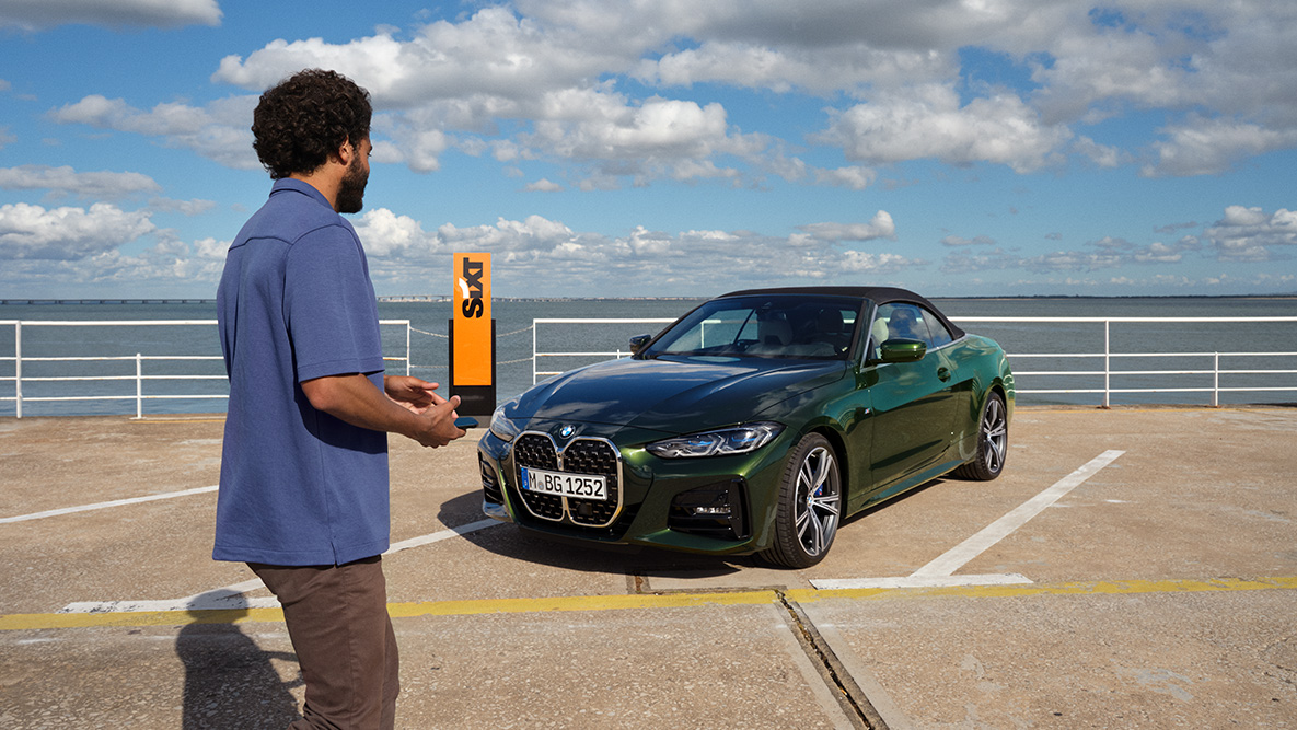 BMW Add-On Mobility App Vídeo BMW Add-On Mobility App Vídeo Hombre con smartphone en la mano delante del BMW Serie 4 Cabrio y anagrama SIXT en el fondo