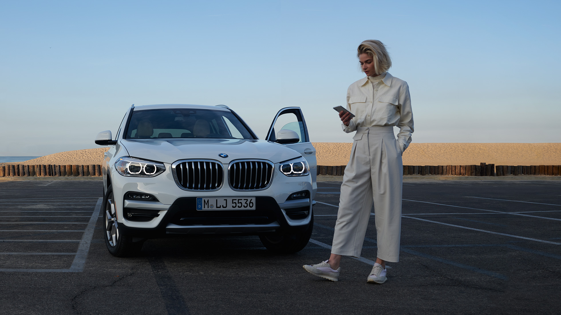 Una mujer usa My BMW App en su smartphone Una mujer usa My BMW App de BMW ConnectedDrive en su smartphone delante de un BMW X5 blanco